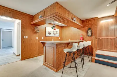 a kitchen with wood paneling and a bar with stools at Lakefront Home with Rooftop Deck, Grill, Games! in Hebron