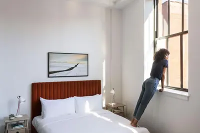a woman is standing on a bed looking out the window at ROOST Cleveland in Cleveland