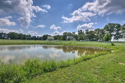 a pond in a field with a house in the background at Renovated Bunkhouse on 12-Acre Horse Farm! in Perrysville
