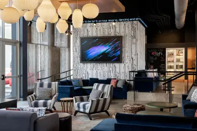 a lobby with blue couches and a tv on a wall at Aloft Beachwood in Beachwood