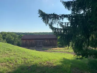 an old barn on a hill in a field at Serene 6BR country home on 325 acres ATV for rent in Burgettstown