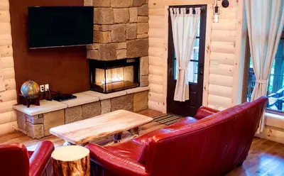 a living room with a fireplace and red leather chairs at Cricket Hill Treehouse by Amish Country Lodging in Millersburg