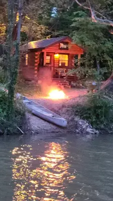 a log cabin with a boat in front of it at River Log Cabins in Waterville