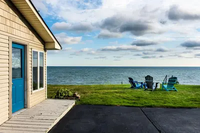 a house with two chairs and the ocean in the background at Cozy Lakefront Cottage in Huron