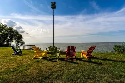 a group of chairs sitting in the grass near the water at Cozy Lakefront Cottage in Huron