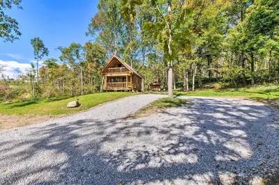 an empty road in front of a log cabin at Peaceful Creekside North Studio with Fire Pit in Holmesville