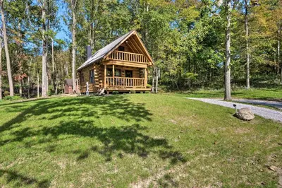 a log cabin in the middle of a grassy field at Peaceful Creekside North Studio with Fire Pit in Holmesville