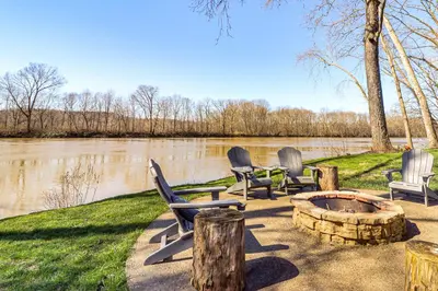 a group of chairs sitting around a fire pit next to a river at Riverfront Zanesville Getaway with Private Bar! in Dresden