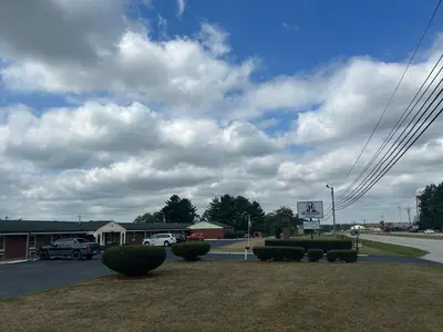 a parking lot with bushes and a cloudy sky at Hillcrest Motel by Oyo Aurora near Lawrenceburg in Aurora