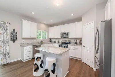 a kitchen with white cabinets and a large island with stools at 1344 soaring way NEW Cheerful 5 bedroom home in quiet suburban area in Maineville
