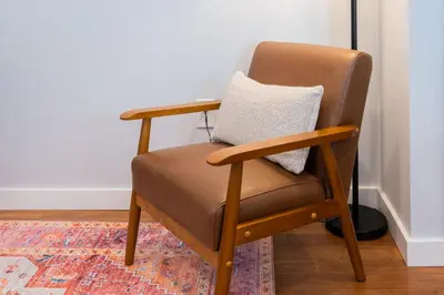 a brown chair with a pillow on a rug at Prime OTR steps to Vine St, Lux Full Bed, Workspace, fast WiFi, 50in Smart TV, Sleeps 3ppl in Cincinnati