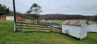a fence and a building in a field with a lake at 100 Acre Red Brick Ranch Hocking Hills Cabin Hot Tub 12 in Logan