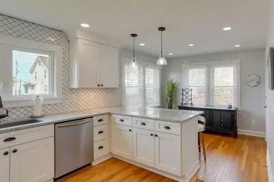 a kitchen with white cabinets and wooden floors and windows at Walk to Lake Erie Chic Home, Private Yard and Deck in Avon Lake