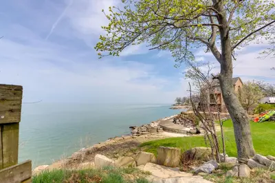 a tree on a hill next to a body of water at Walk to Lake Erie Chic Home, Private Yard and Deck in Avon Lake