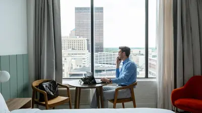 a man sitting at a table with a laptop in front of a window at Dayton Vitality Hotel - Downtown in Dayton